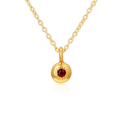 Gold necklace with a round pendant featuring a red gemstone on a white background