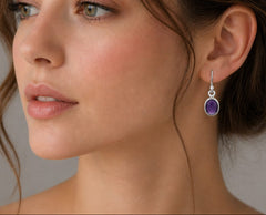 Close-up of a woman wearing purple gemstone earrings with a neutral background