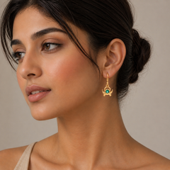 Woman wearing a gold earring with a green gemstone on a neutral background