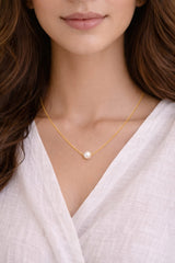 Close-up of a person wearing a gold necklace with pearls on a plain background