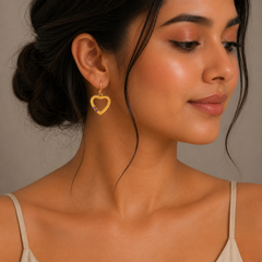 Woman wearing a gold heart-shaped earring with a neutral background