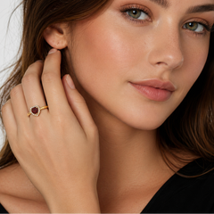 Close-up of a woman wearing a gold ring with a red gemstone, touching her ear.