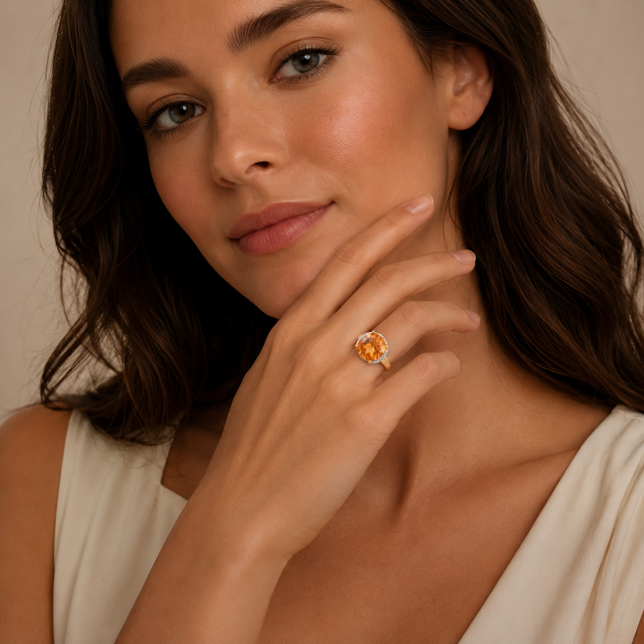 Woman wearing a ring with an orange gemstone against a neutral background