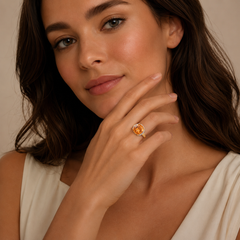 Woman wearing a ring with an orange gemstone against a neutral background