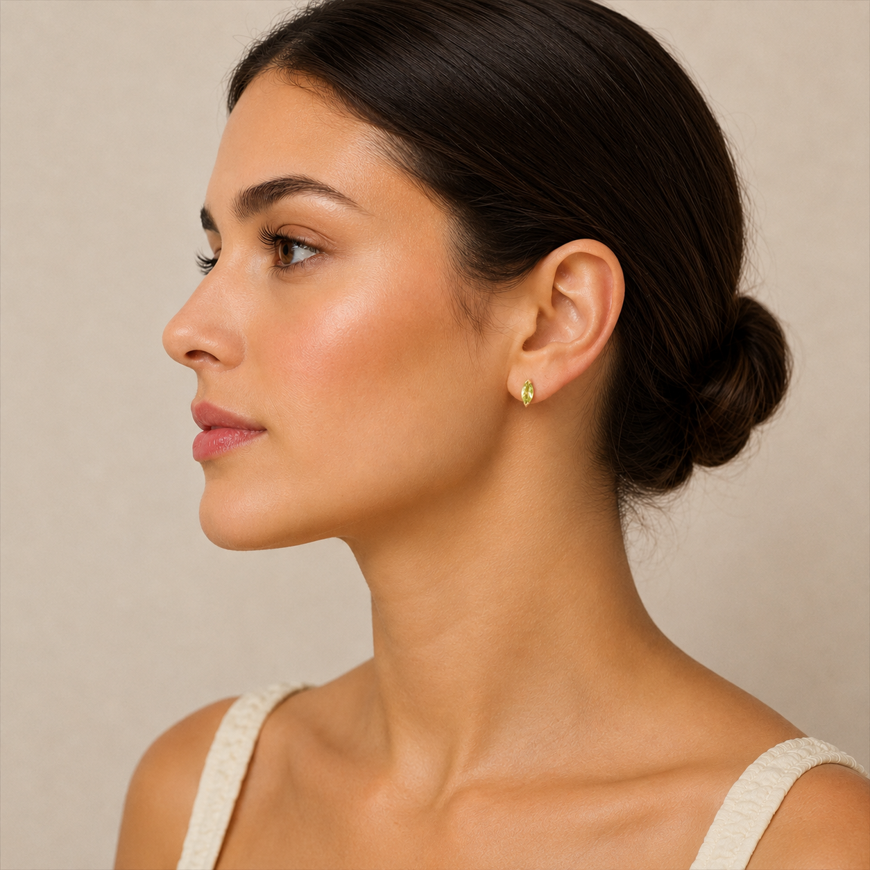 Woman wearing a gold earring with a green gemstone against a neutral background