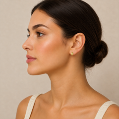 Woman wearing a gold earring with a green gemstone against a neutral background