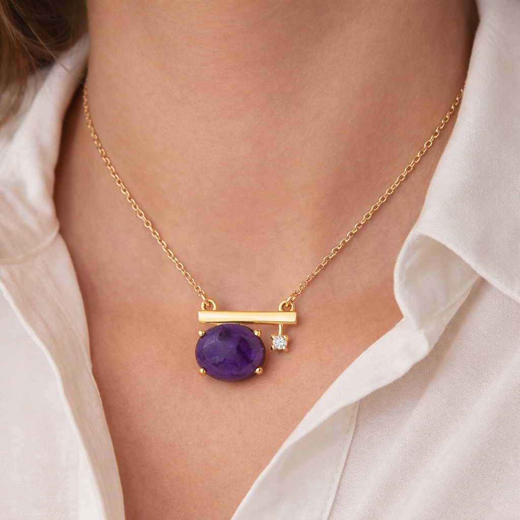 Gold necklace with a purple gemstone and diamond on a person wearing a white shirt.