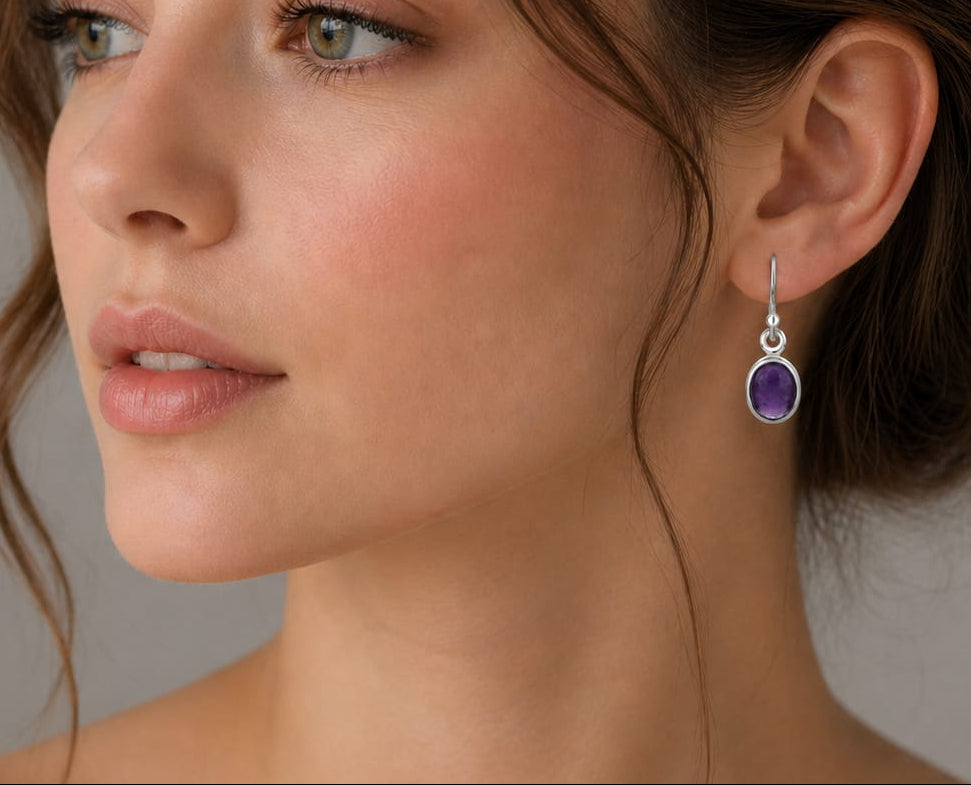 Close-up of a woman wearing purple gemstone earrings with a neutral background