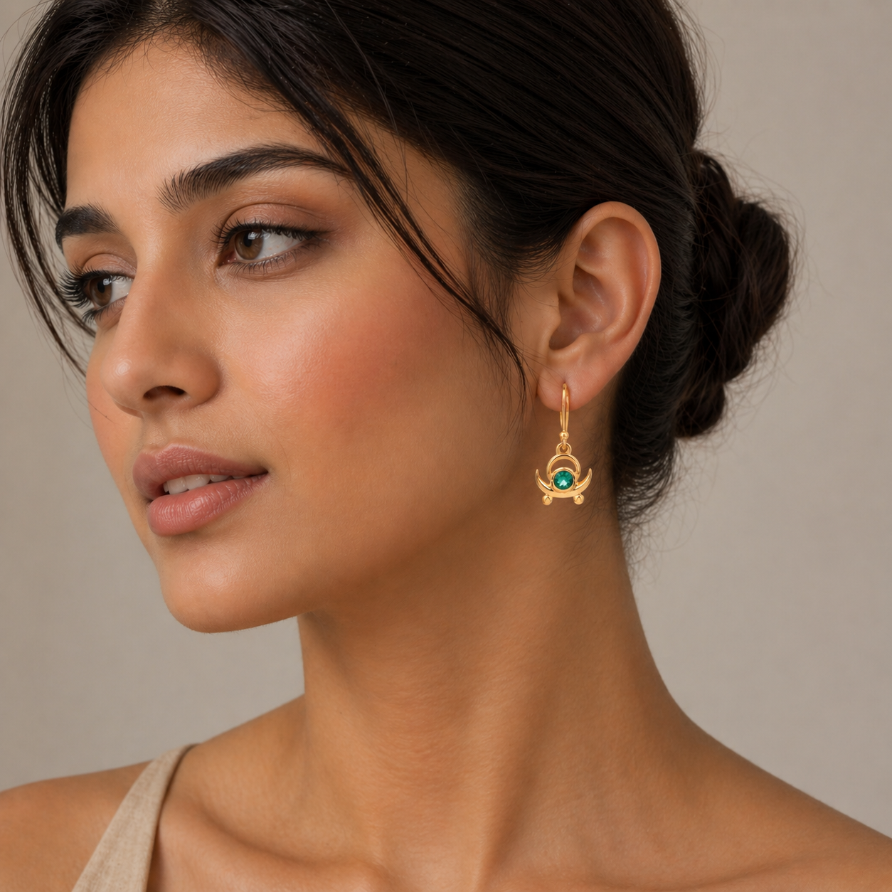 Woman wearing a gold earring with a green gemstone on a neutral background
