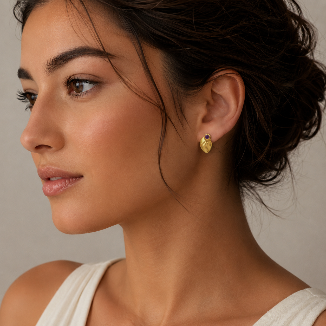 Close-up of a woman wearing gold earrings with a neutral background