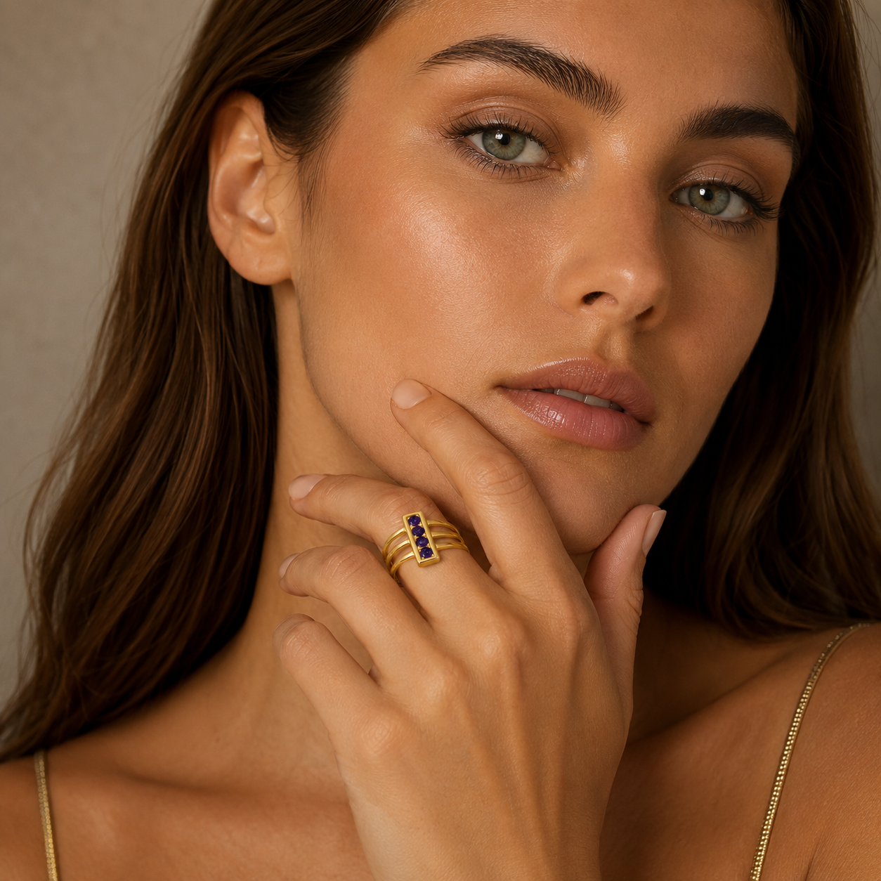 Close-up of a woman wearing a gold ring with gemstones, against a neutral background.
