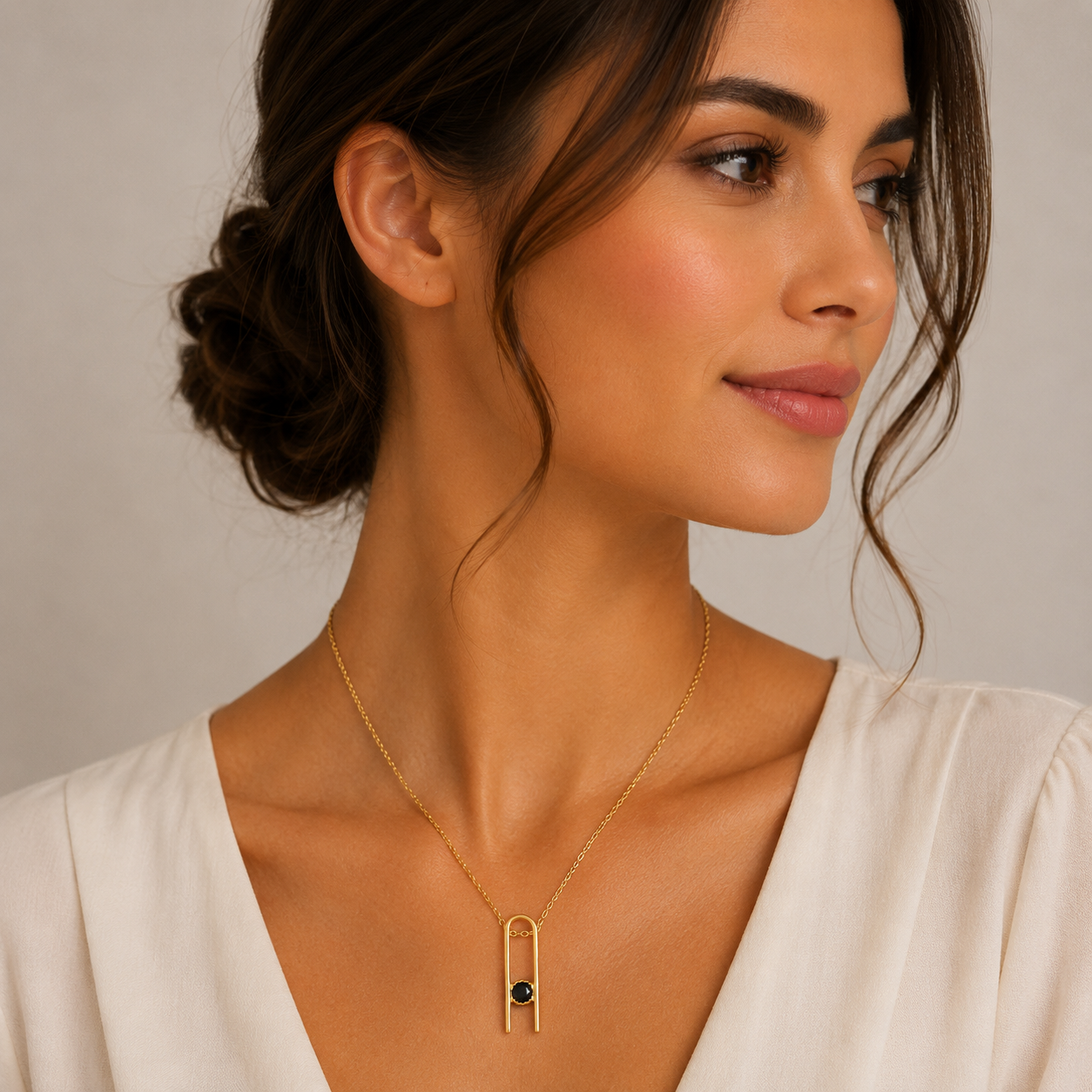 Woman wearing a gold necklace with a black gemstone against a neutral background