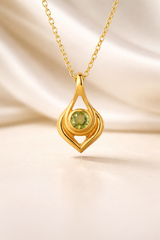 Gold pendant with a green gemstone on a beige background