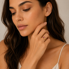Woman wearing a gold ring with a pink gemstone, touching her neck.