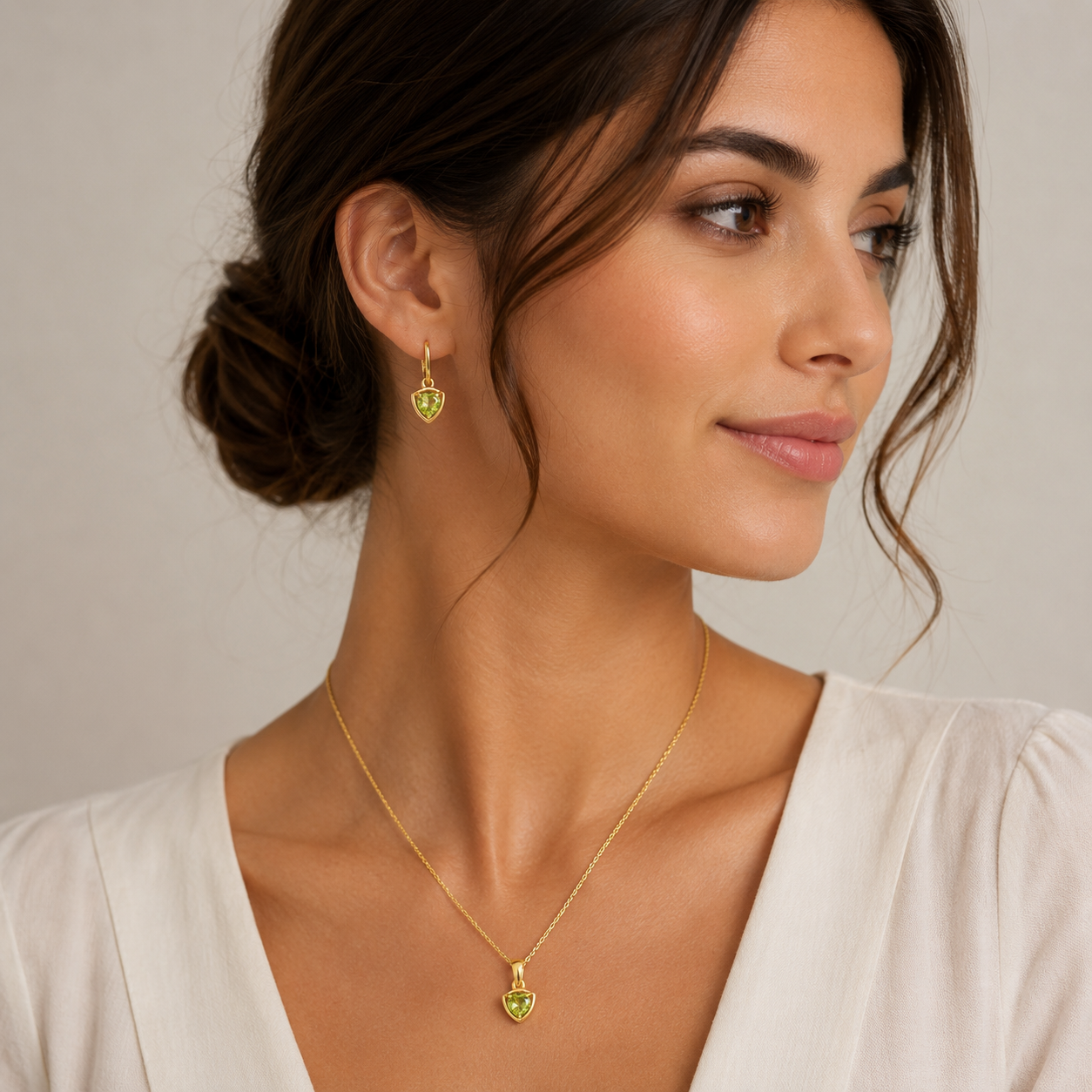 Woman wearing a gold necklace and earrings against a neutral background